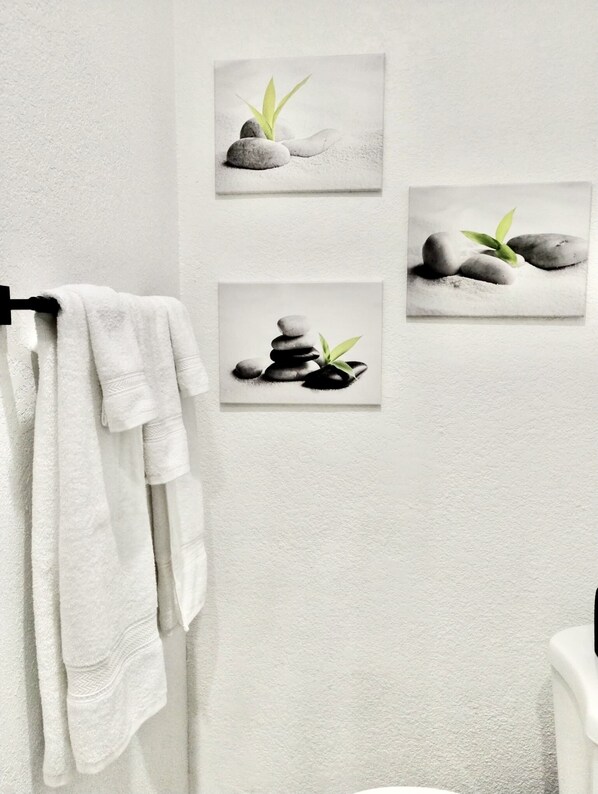 A bathroom with a towel rack holding a white towel, three framed pictures of stones and leaves on the wall, and a white bathtub.