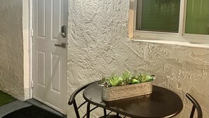 En terrasse med et bord og stole, en potteplante, en dør og en væg med struktur.