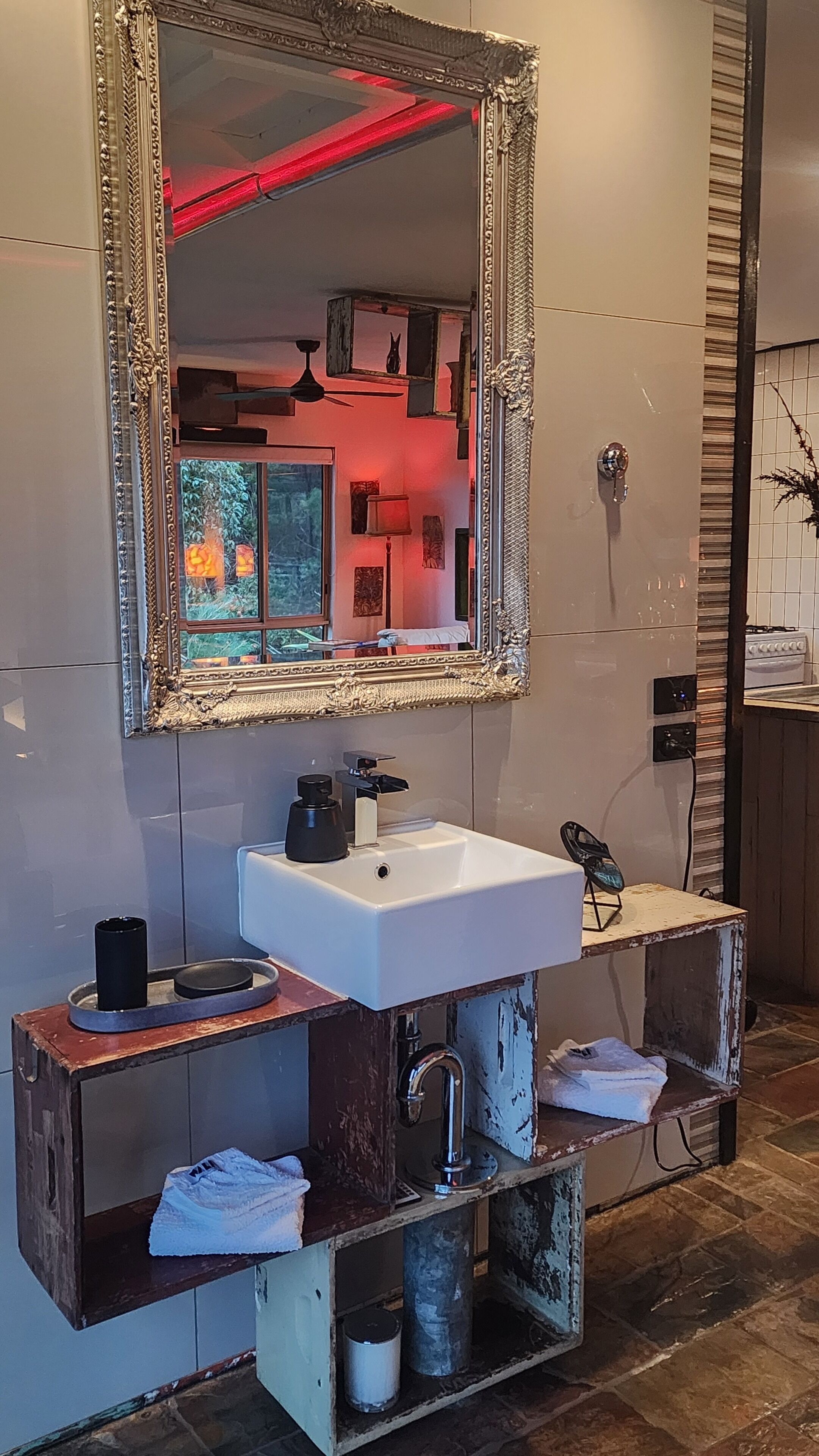 Une salle de bain avec un lavabo blanc, un grand miroir décoratif et un meuble-lavabo en bois.