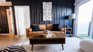 Ein modernes Wohnzimmer mit einem braunen Ledersofa, einem Holztisch und einem weißen Teppich mit Struktur.