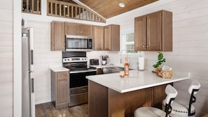 A modern kitchen with wooden cabinets, stainless steel appliances, a central island, and a small seating area. - Waterfront Luxury Tiny Home 360 North on Wilson Lake Close to Robert Trent Jones (Muscle Shoals)