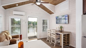 A modern kitchen with white cabinetry, a wooden ceiling, and a view of a lake through the sliding glass doors. - Waterfront Luxury Tiny Home 360 North on Wilson Lake Close to Robert Trent Jones (Muscle Shoals)