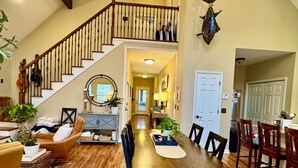 Un comedor espacioso con una mesa y sillas de madera, una escalera que lleva a un nivel superior y un tapiz decorativo.