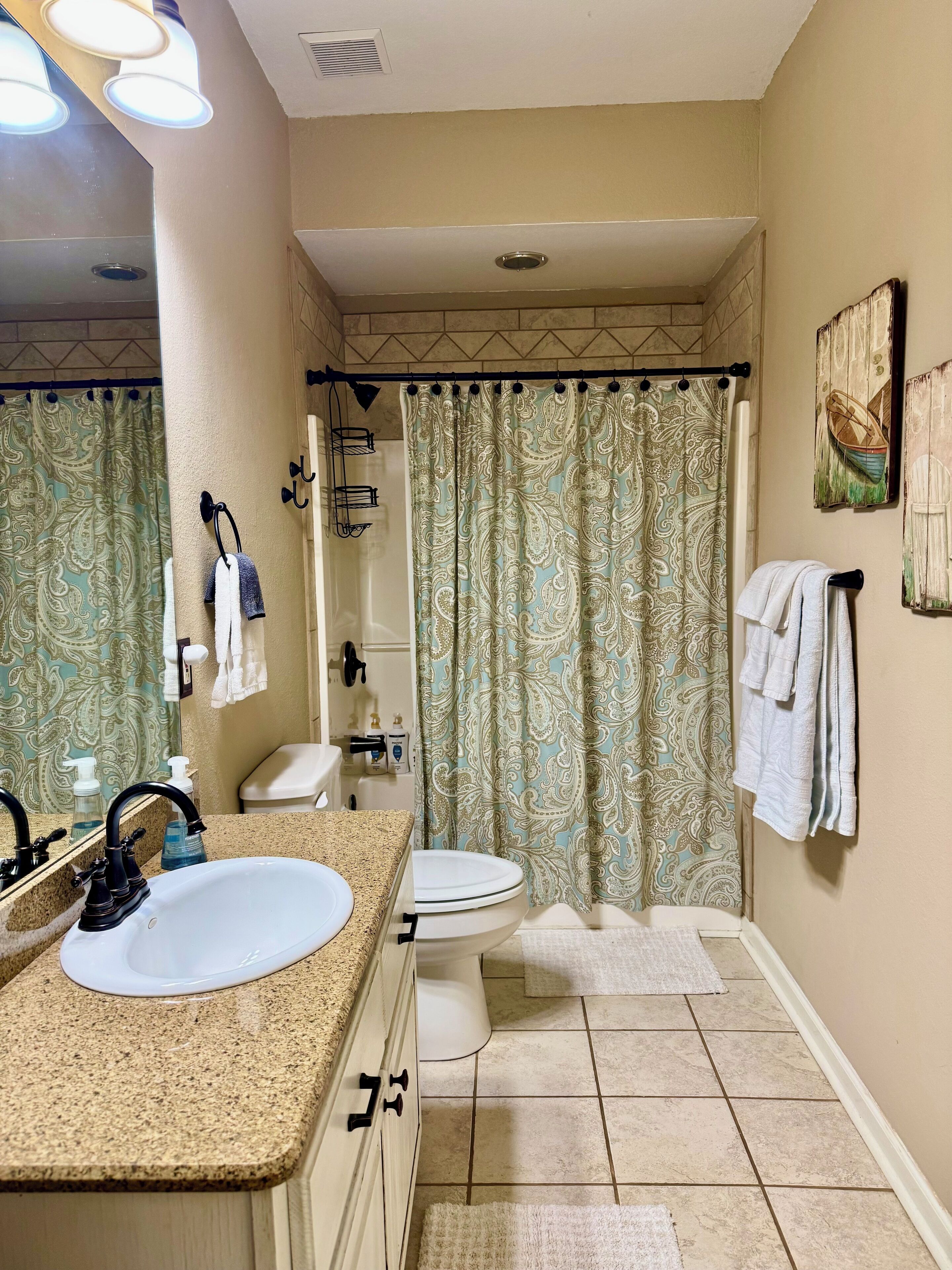A bathroom with a sink, toilet, and shower curtain. There are towels hanging on the wall and a mirror above the sink.
