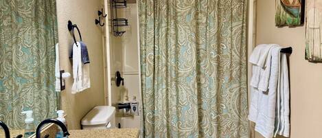 A bathroom with a sink, toilet, and shower curtain. There are towels hanging on the wall and a mirror above the sink.