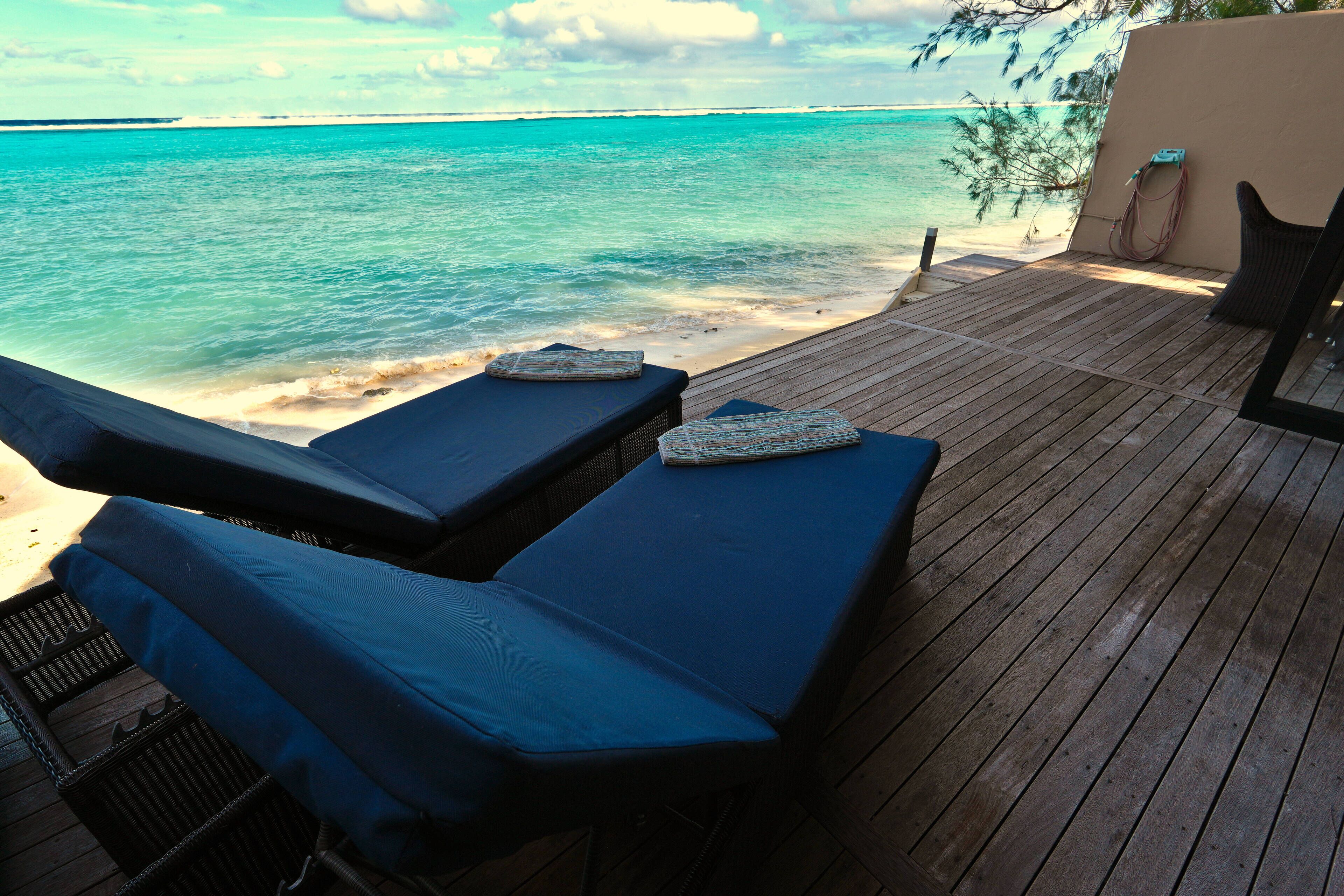 A wooden deck with two lounge chairs facing the ocean.