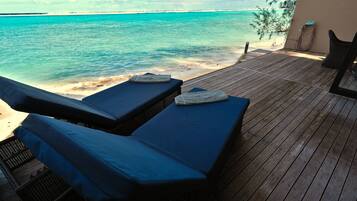 A wooden deck with two lounge chairs facing the ocean.
