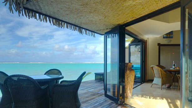 A wooden deck with wicker furniture, a glass door leading to a room, and a view of the ocean.