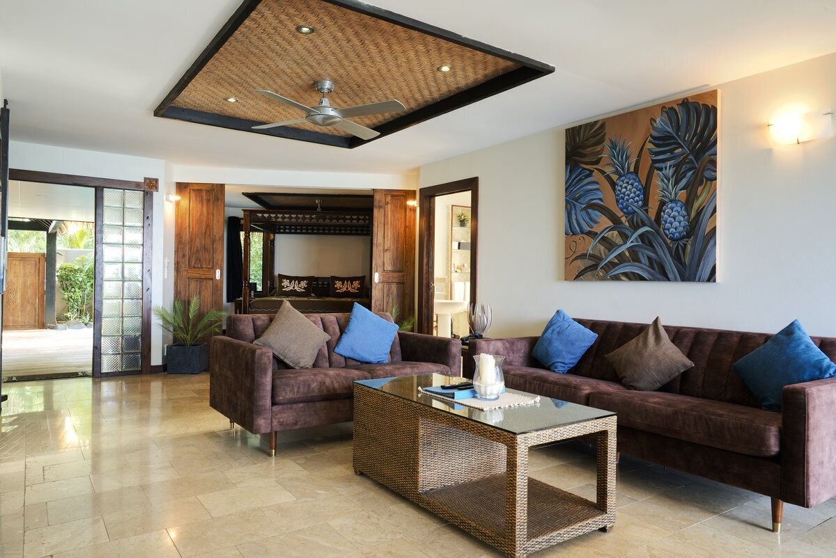 A spacious living area with a ceiling fan, two sofas with cushions, a coffee table, and a large painting on the wall.