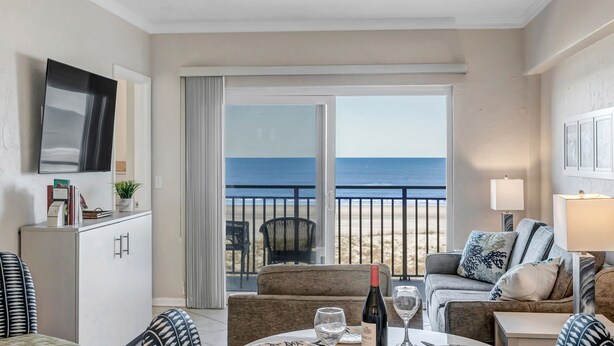Habitación de hotel con balcón, sofá, mesa de comedor y televisor.