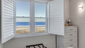 Una habitación con un ventanal grande con vista a la playa, un banco de madera y un aparador con cajones.