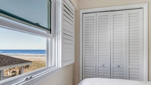 Un dormitorio con vista a la playa, una cama blanca y un armario blanco con puertas persianas.