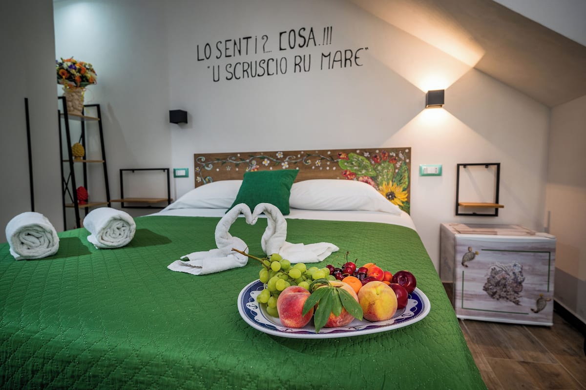 A neatly made bed with a green bedspread, a plate of fruit, and towels arranged in a heart shape.