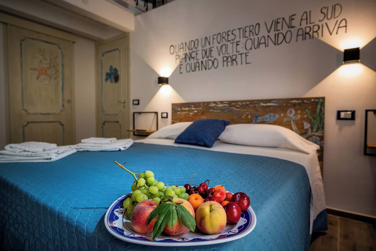 A neatly made bed with a blue bedspread, a fruit plate on the bed, and a wall with a Spanish phrase.