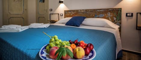A neatly made bed with a blue bedspread, a fruit plate on the bed, and a wall with a Spanish phrase.
