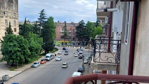 Un balcone con ringhiera in ferro battuto che si affaccia su una strada trafficata, con auto e palazzi.
