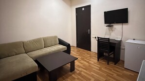 Un soggiorno con divano, tavolino, televisore a parete e un piccolo frigorifero.