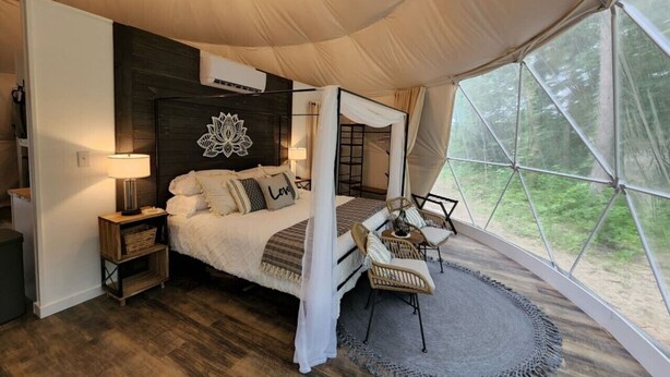 A tent-style bedroom with a bed, bedside tables, a chair, and a view of the outdoors.