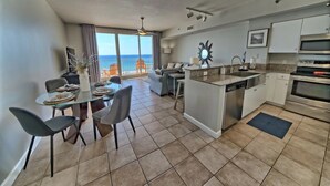 A modern kitchen with a central island, a dining area with a glass table, and a view of the ocean through large windows.