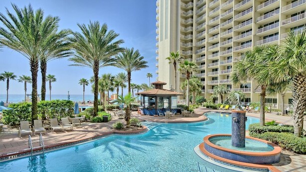 A hotel pool area with palm trees, lounge chairs, and a view of the ocean.