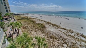 A beach view with a pier, palm trees, and a high-rise building.