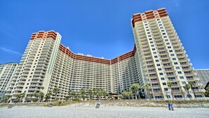 A high-rise hotel with multiple balconies, a beachside location, and a clear blue sky.