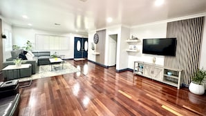 Een moderne woonkamer met een houten vloer, een grijze bank en een televisie op een houten dressoir.