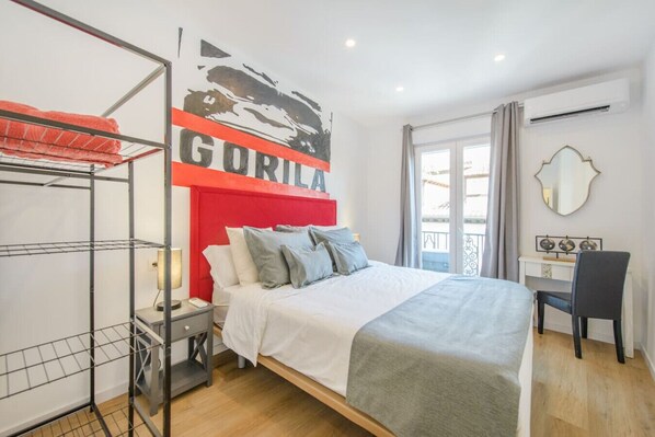 A bedroom with a bed, a desk, a chair, a wardrobe, and a large window.