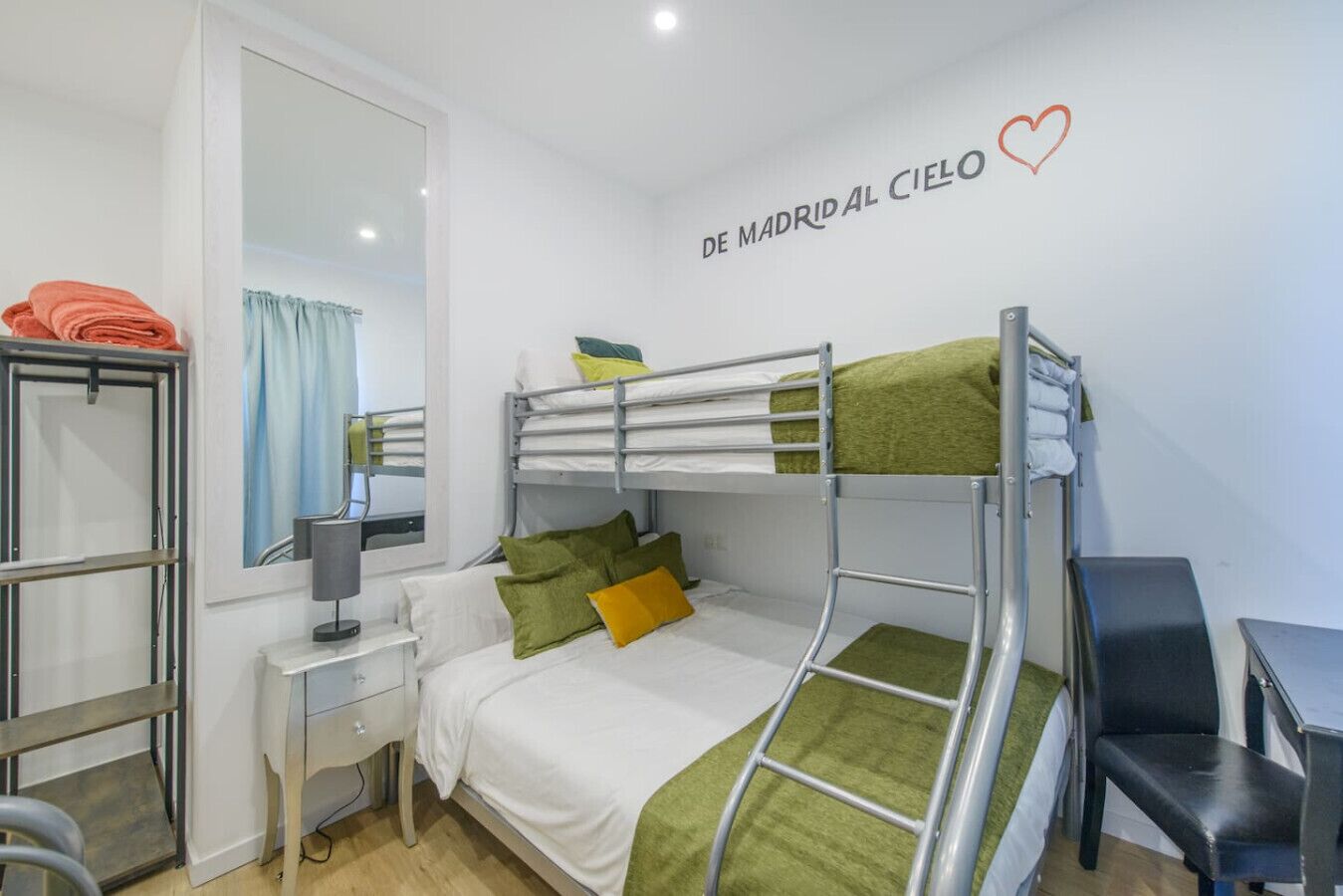 Habitación con literas, escritorio, silla y espejo.
