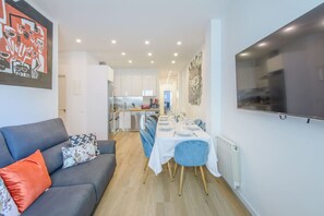 A modern apartment with a living room, dining area, kitchen, and a large TV mounted on the wall.