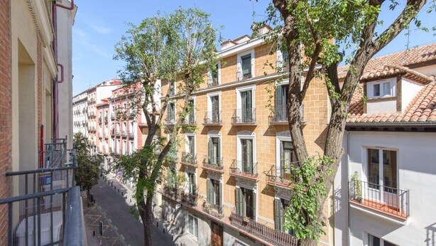 A row of multi-story buildings with balconies, a clear sky, and trees in the foreground. - Top groups MALASAñA, by MoNARO (Centro)