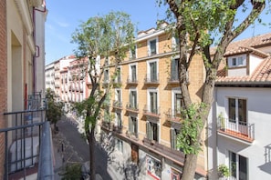 A row of multi-story buildings with balconies, a clear sky, and trees in the foreground.
