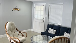 Una sala de estar con una silla de mimbre, una mesa de centro de vidrio, un sofá azul oscuro y un letrero que dice 'Welcome' en la pared.