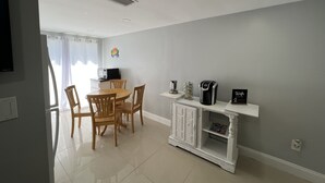 Una cocina moderna con comedor, muebles de cocina blancos y una cafetera.