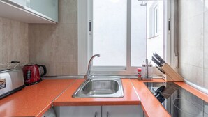 A kitchen with a stainless steel sink, a red electric kettle, a toaster, and a window with a view of the outside. - Centro Historico MAD. 2BR 1BTH (Madrid)