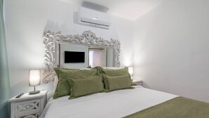 A bedroom with a large bed, green pillows, a white headboard, a flat-screen TV, and an air conditioning unit. - Centro Historico MAD. 2BR 1BTH (Madrid)