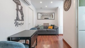 A modern living room with a grey sofa, a small table, and a wall-mounted clock. - Centro Historico MAD. 2BR 1BTH (Madrid)