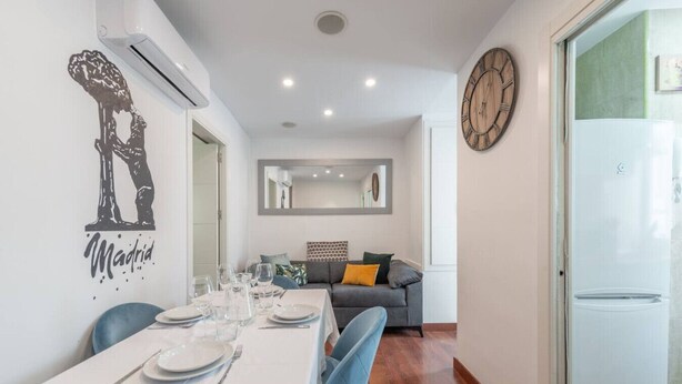 A dining area with a table set for four, a grey sofa, and a large wall clock. - Centro Historico MAD. 2BR 1BTH (Madrid)