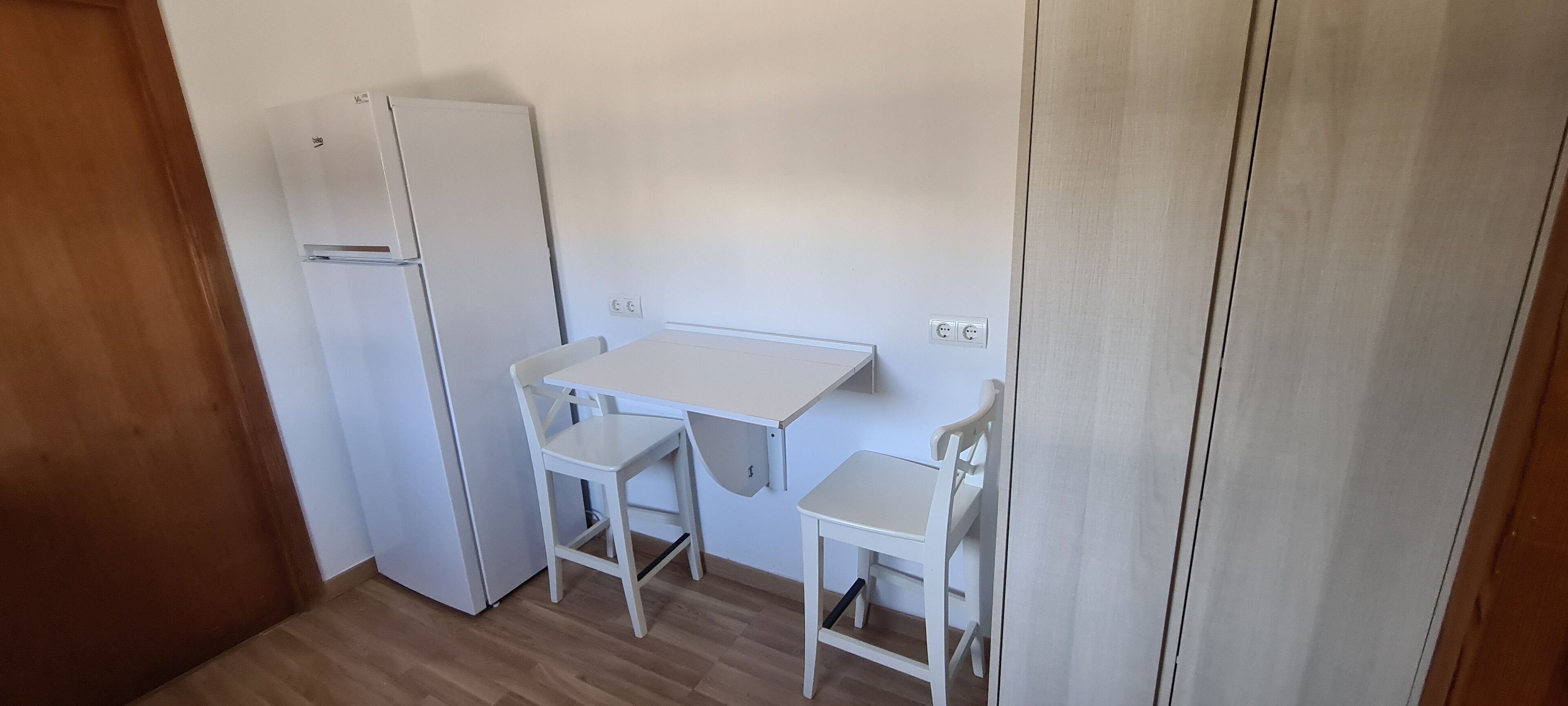 A small kitchenette with a white refrigerator, a white table, and two white chairs.
