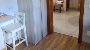 Ein Zimmer mit Holzboden, einem weißen Schreibtisch mit Stuhl, einem hölzernen Bogen und einem weißen Vorhang.