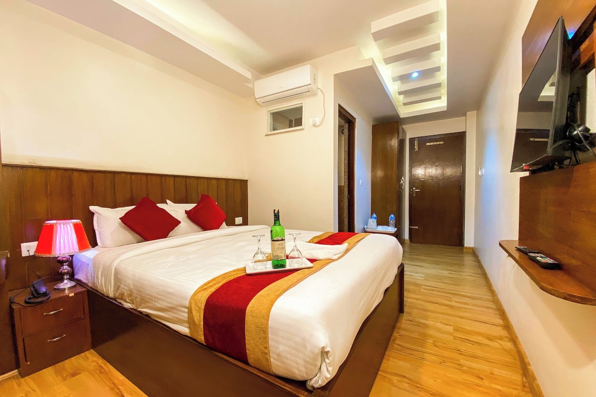 A hotel room with a large bed, a bedside table with a lamp, a bottle of champagne, and a tray with glasses.