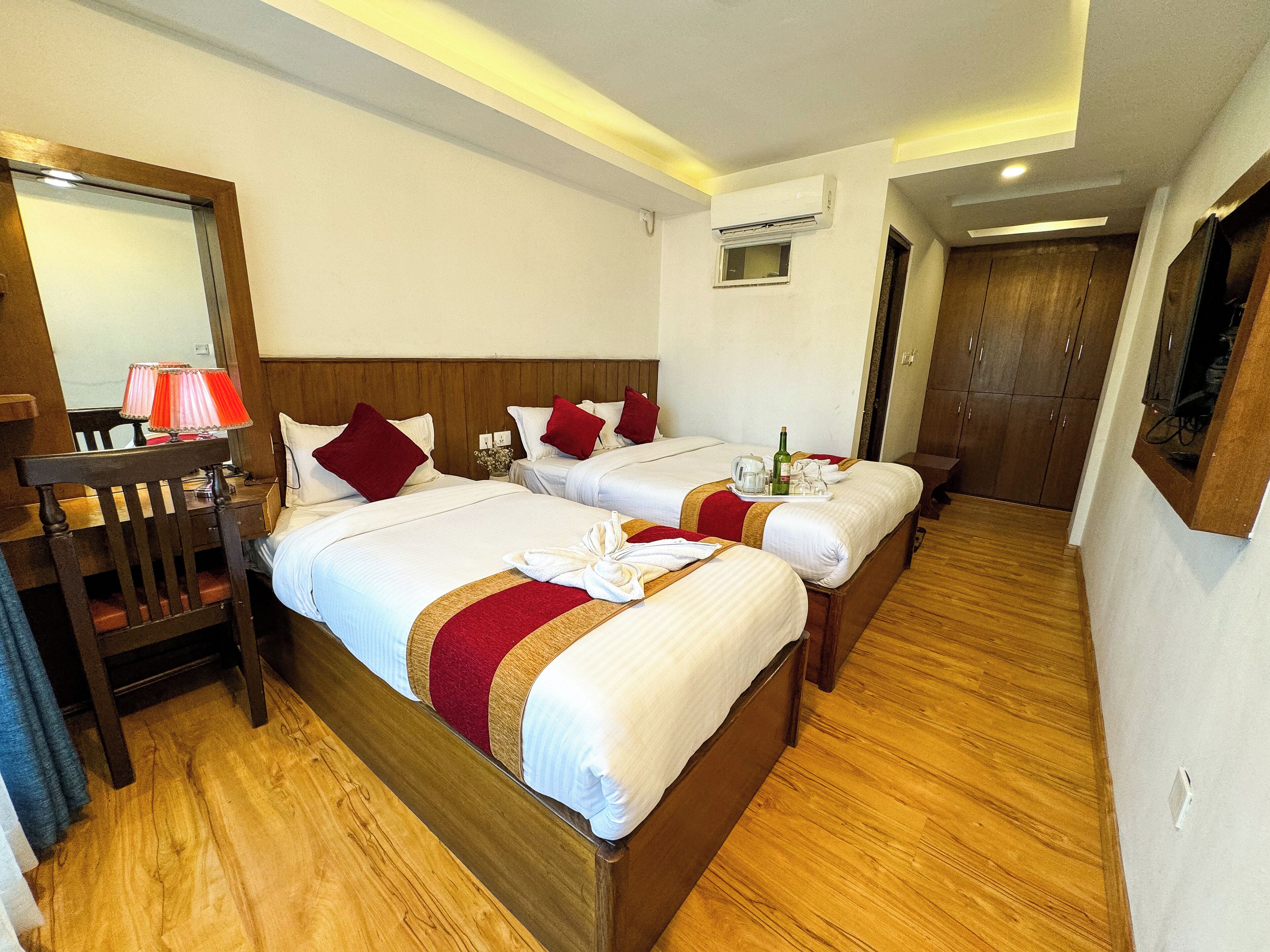 Habitación de hotel con dos camas, cabeceros de madera, un escritorio con lámpara y un espejo.