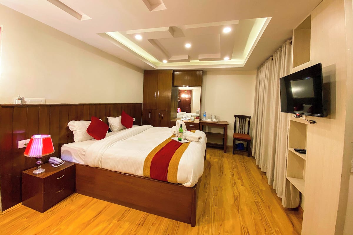 A hotel room with a wooden bed, bedside table, lamp, TV, and a desk with a chair.