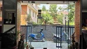 A modern hotel entrance with a glass door leading to a parking area. There are potted plants and a blue scooter parked outside. - Hotel Abi International (Kathmandu)