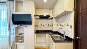 A compact kitchen with wooden cabinets, a black countertop, a stainless steel sink, and a built-in TV. - Hotel Abi International (Kathmandu)