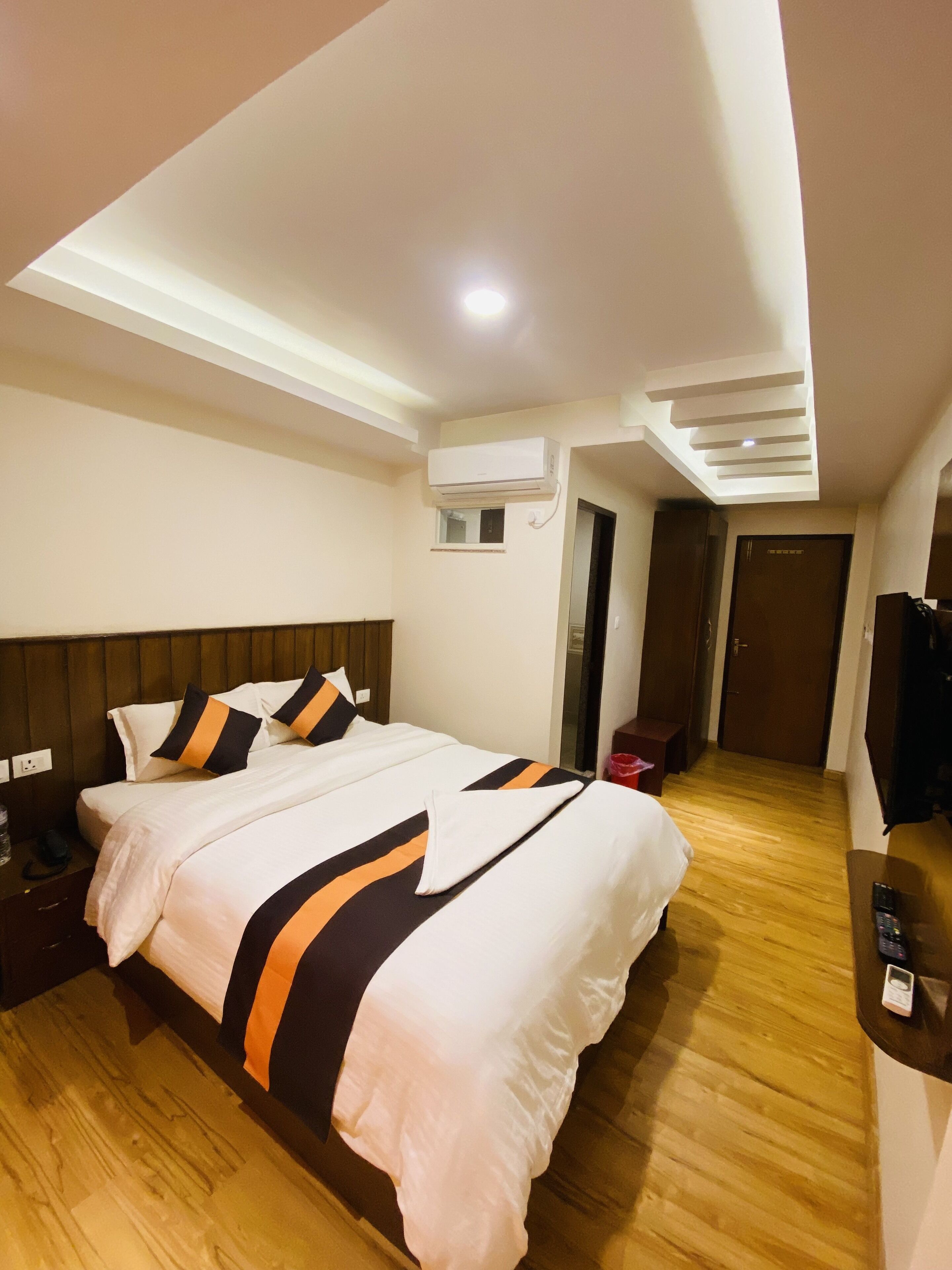 A hotel room with a large bed, wooden flooring, a flat-screen TV, and an air conditioning unit.