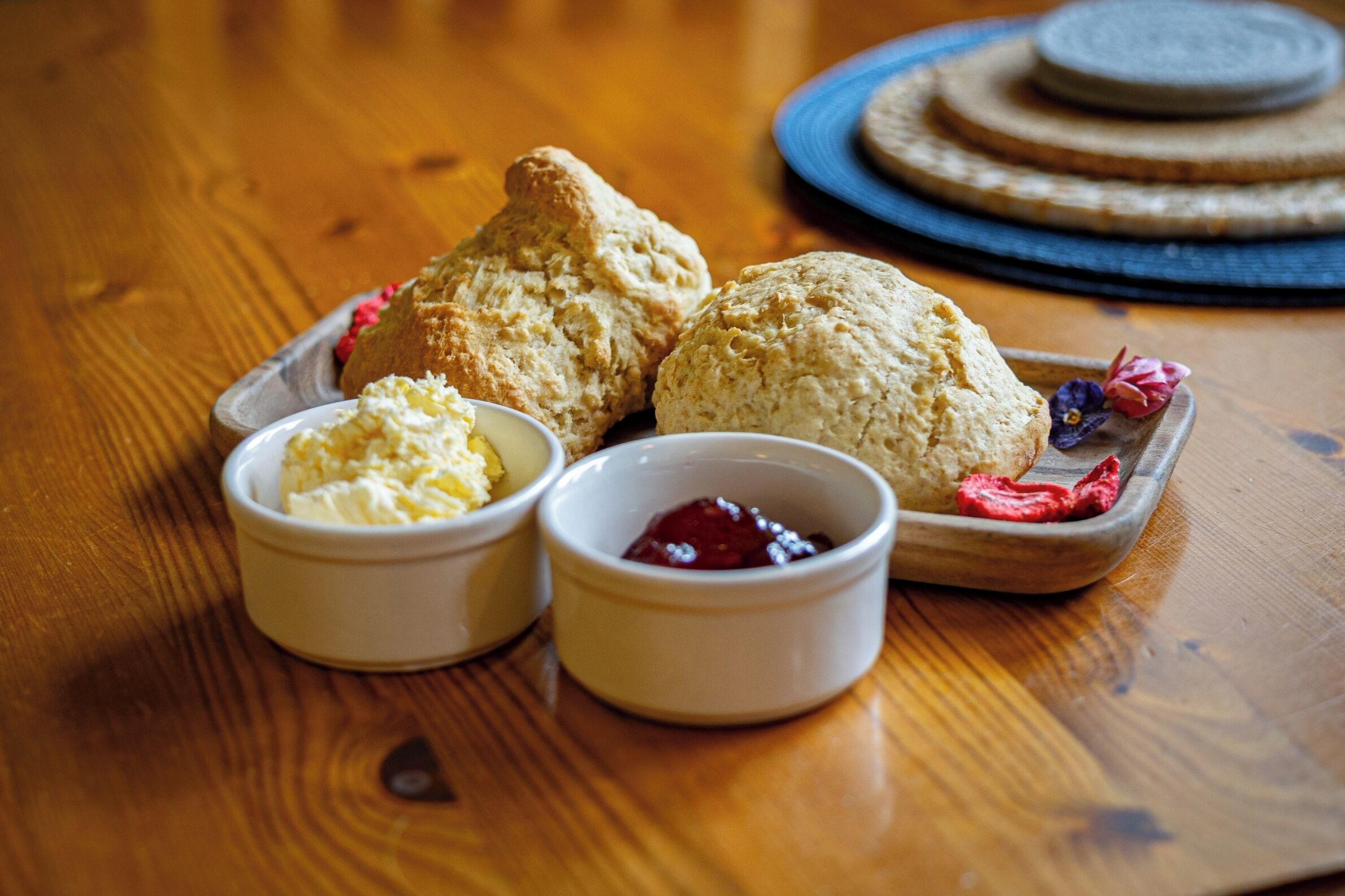 A wooden table with three scones and two small bowls of butter and jam.
