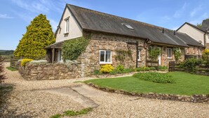 A stone house with a sloped roof, a gravel driveway, and a well-maintained lawn.