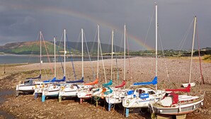 A row of boats docked on a rocky shore with a rainbow in the background.