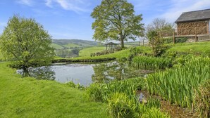 A serene landscape with a pond, lush greenery, and a wooden gazebo.